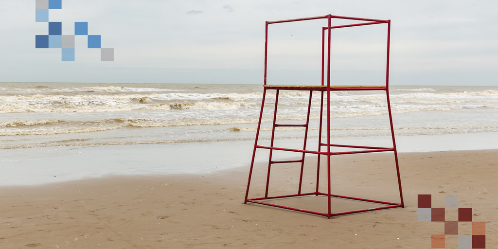 Weitläufiger Strand zu sehen, im Hintergrund das Meer mit einigen Wellen. Im Vordergrund ist ein roter, Metallhochsitz für die Rettungsschwimmer. Es sind keine Menschen auf dem Foto zu sehen.