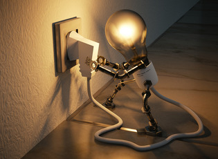 Eine Figur, die aus einer Glühlampe und Armen und Beinen aus Metall zusammengesetzt ist, steckt das mit ihr verbundene Stromkabel in eine Steckdose ein.