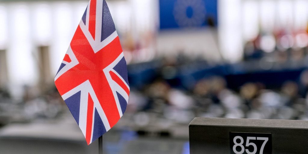 In the European Parliament in Strasbourg, a small British flag is standing on the desk of a member of Parliament. The parliament speaker's podium and the large EU flag above it can be seen in the background.