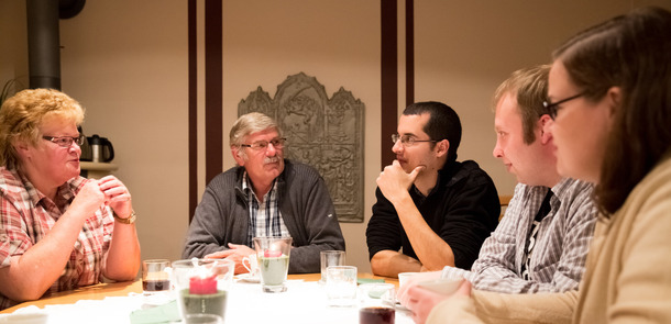 Mehrere Menschen sitzen um einen Tisch herum und besprechen diverse Themen.