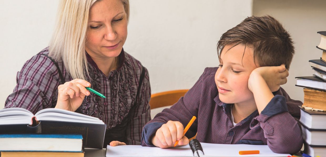 (© dimaberkut / iStockphoto.com) Eine Frau und ein Junge sitzen an einem Tisch. In ihren Händen halten sie einen Stift und blicken gemeinsam auf vor ihnen liegende Bücher und Zettel.