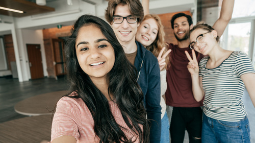 Mehrere junge Menschen nehmen mit einem Handy ein gemeinsames Selfie auf und lächeln in die Kamera.
