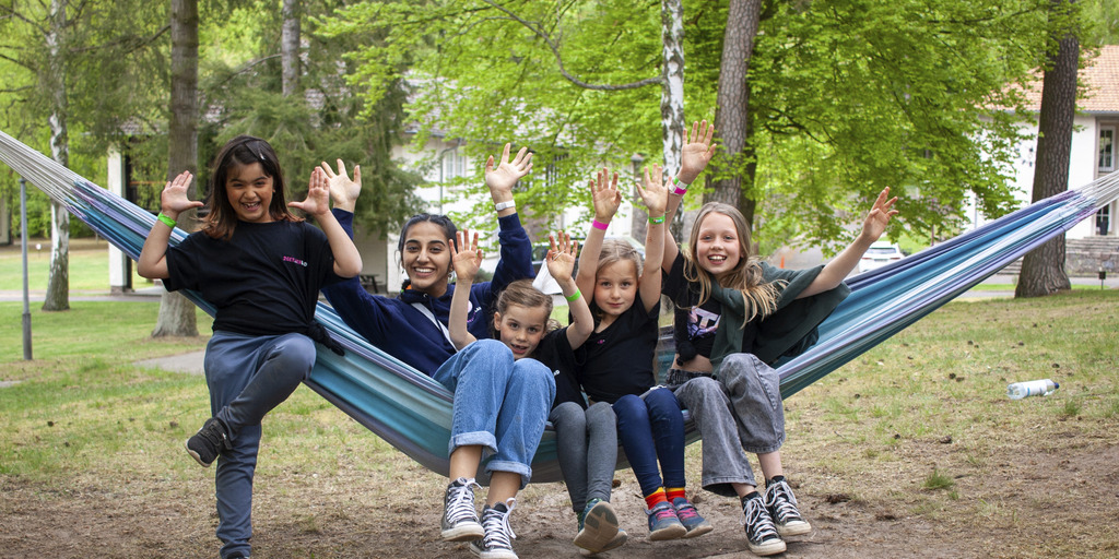 Kinder sitzen in einer Hängematte und lachen in die Kamera.