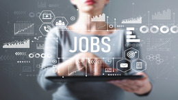 Frau steht hinter transparenter Scheibe auf der mittig Jobs steht und Daten und Zahlen aufgeschrieben sind