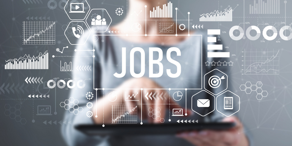 Frau steht hinter transparenter Scheibe auf der mittig Jobs steht und Daten und Zahlen aufgeschrieben sind