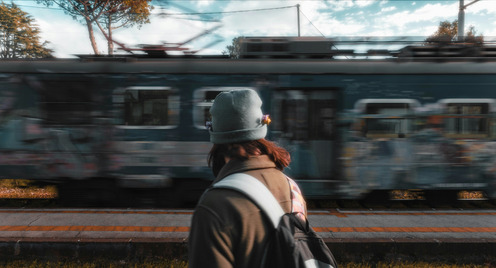 Junge Frau mit Mütze steht vor einem vorbeifahrendem Zug.