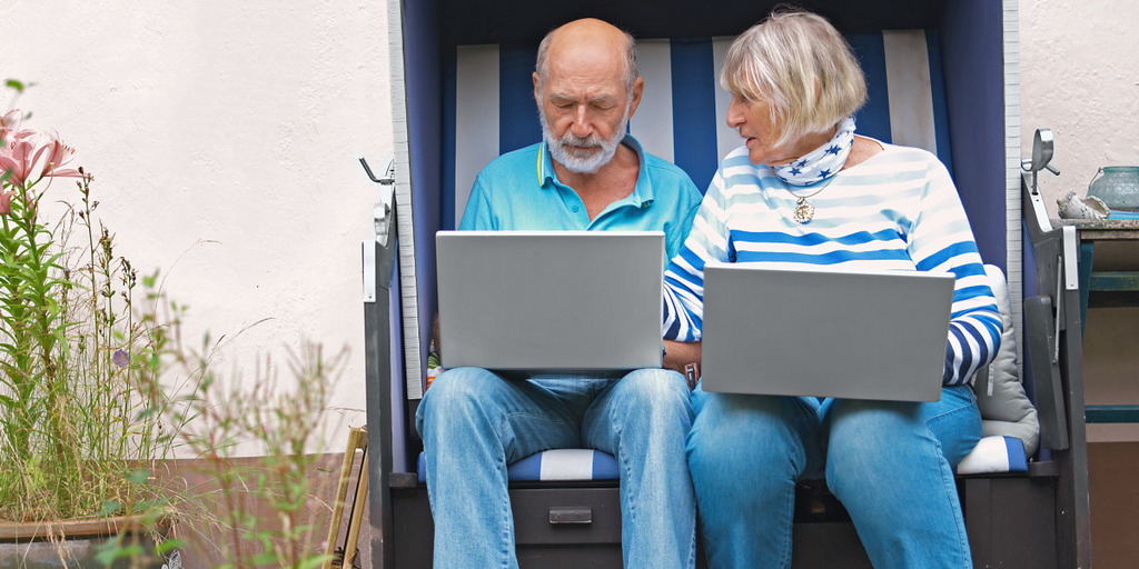 Ein älteres Paar sitzt in einem Strandkorb mit Laptops auf dem Schoß.