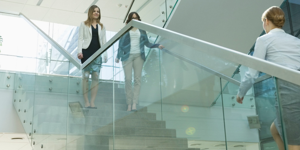 Zwei Frauen stehen auf einer Treppe. Auf dieser kommt ihnen von unten eine dritte Frau entgegen.