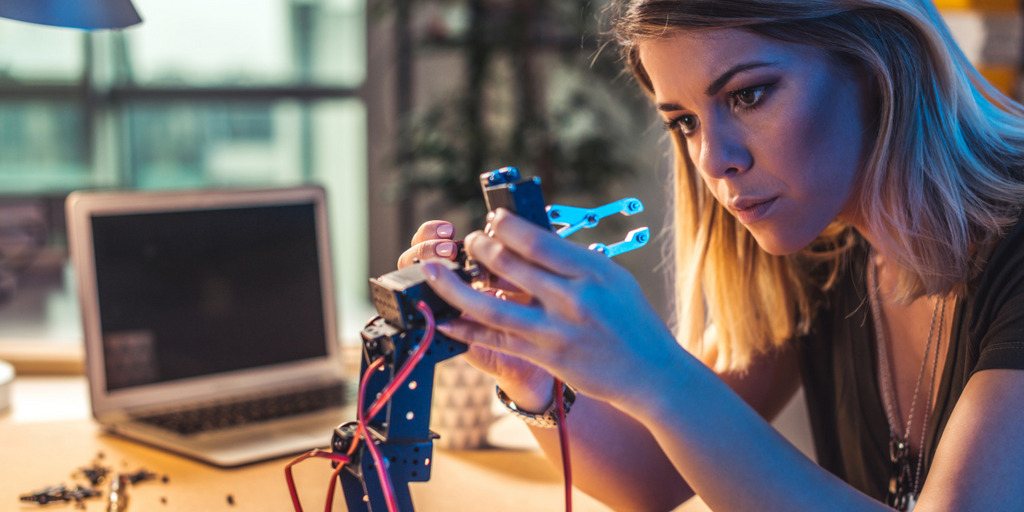 Junge Frau arbeit in einem Werkraum für Technik an einer Roboterhand.