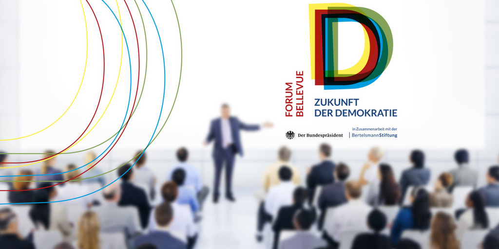 Über einem Publikum, das einem nur unscharf dargestellten Redner zuhört, ist das Logo des "Forums Bellevue - Zukunft der Demokratie" zu sehen.