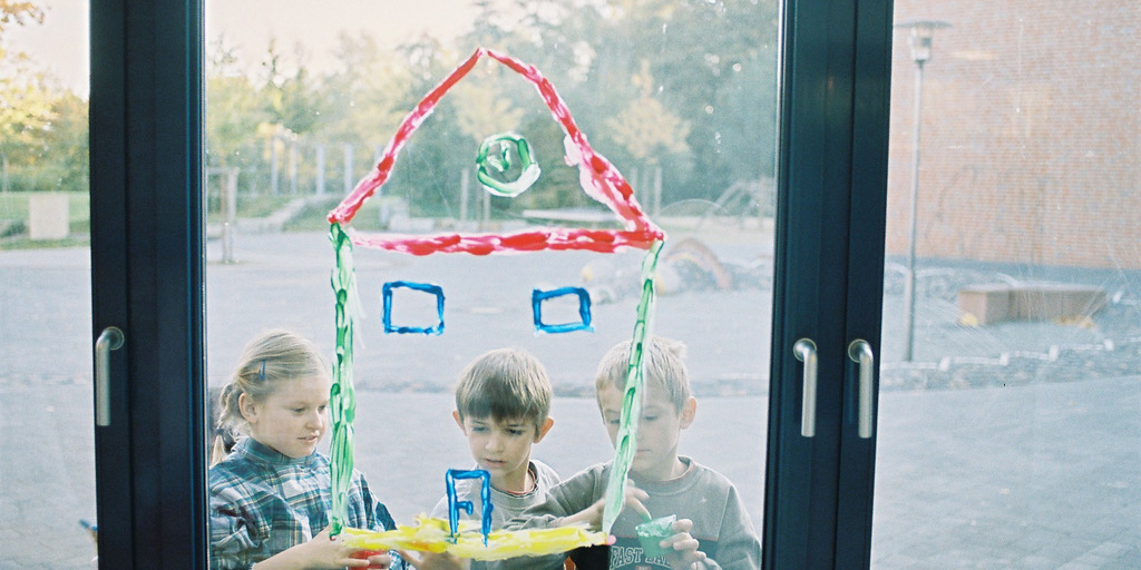 Kinder malen mit Farbe ein Bild auf dem Fenster