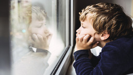 Porträt eines Jungen, der gelangweilt aus dem Fenster seines Zimmers schaut.