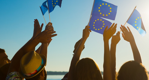 People with raised hands waving flags of the European Union.