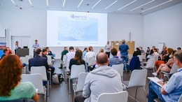 Blick von hinten im Raum auf die Teilnehmerinnen des Open-Data-BArcamps 2021 in Bochum. Vorne sind die Moderatoren und Gastgeber und eine Begrüßungsfolie ist an die Wand geworfen.