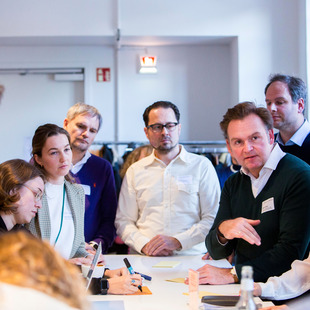 Teilnehmende des Workshops am 24.11.24 sitzen um einen Tisch herum und diskutieren