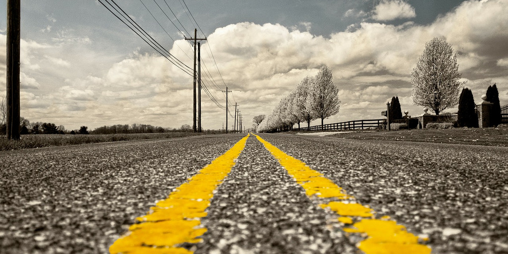 Der Blick zeigt eine Straße. Auf der Straße sind zwei gelbe Streifen gemalt, die bis in den Horizont reichen.