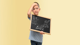 Ein Junge steht vor einer gelben Wand, er hat eine kleine Tafel in der Hand