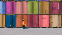 Engineer man with yellow crash helmet and worker west checking cargo freights in front of colorful cargo container stacks in shipping port.