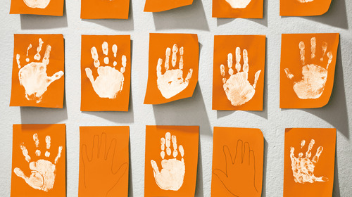 Abdrücke von Kinderhänden auf orange-farbene Klebezetteln.