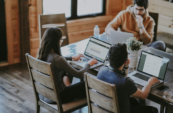 Junge Menschen sitzen gemeinsam am Schreibtisch und arbeiten an ihren Laptops