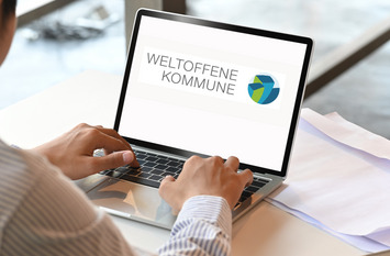 Auf einem Laptop sieht man das Logo der Wissensplattform Weltoffen Kommune. Vor dem Laptop sitzt eine Person.