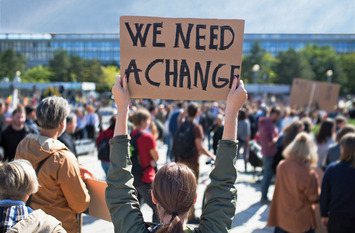Frau hält ein Schild hoch, auf dem "We need change" drauf steht.