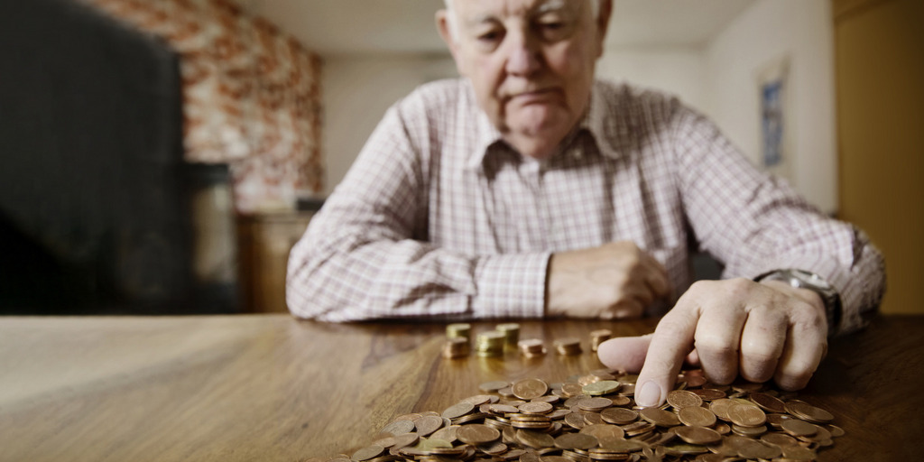 Ein älterer Mann sitzt an einem Holztisch, auf dem er sein Münzgeld zählt.