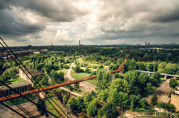 Durch den Landschaftspark Nord in Duisburg läuft mitten durch eine grüne Landschaft mit Bäumen, Sträuchern und Wiesen zwei rostige Röhren, die zu dem ehemaligen Hüttenwerksgelände führen.