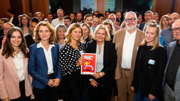 Group picture of German Federal Minister of the Interior Nancy Faeser, Bertelsmann Stiftung Executive Board member Daniela Schwarzer and members of the Citizens' Assembly during the event at which the "Forum against Fakes" were submitted. Nancy Faeser and a member of the Citizens' Assembly are surrounded by the other participants and present the recommendations to the camera.