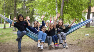 Kinder sitzen nebeneinander in einer Hängematte und lachen in die Kamera.