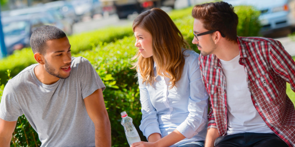 Three young people sit on a park bench and discuss.
