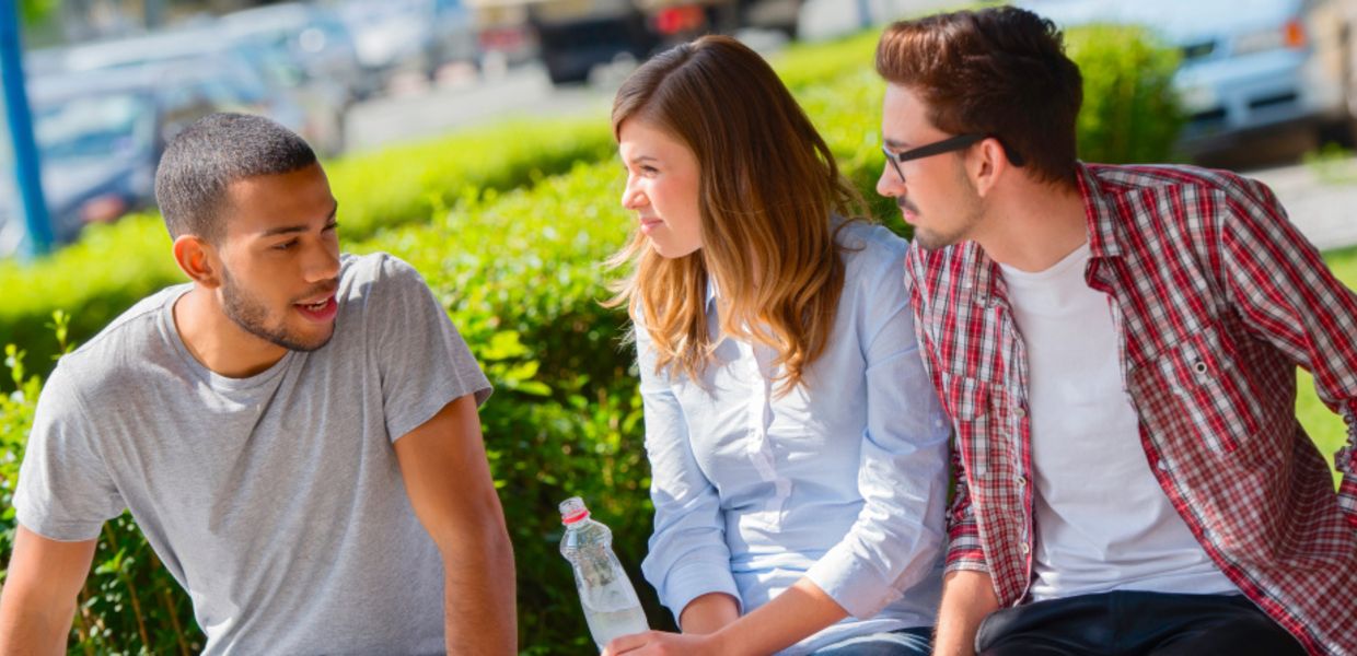 (© vm / iStockphoto.com) Three young people sit on a park bench and discuss.