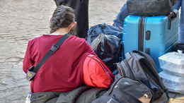 Frau mit Rückenansicht sitzt inmitten von Gepäck und