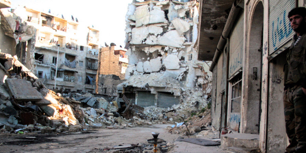 Blick auf ein teilweise zerstörtes Wohngebiet im syrischen Aleppo. Rechts steht ein Mann und betrachtet die Zerstörungen.