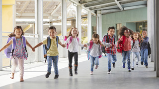 Grundschulkinder rennen händchenhaltend durch den Korridor.