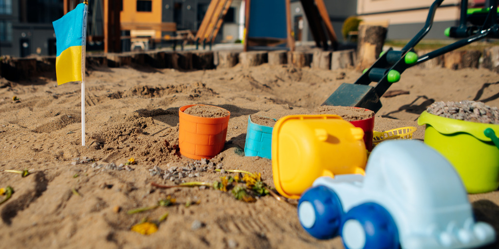 Sandkasten mit Spielzeug und kleiner Ukraineflagge