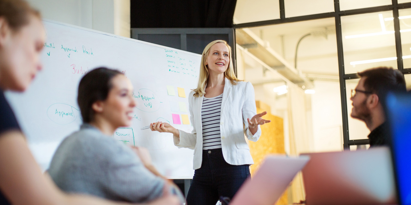 [Translate to English:] Frau präsentiert vor Whiteboard in einer Besprechungsszene