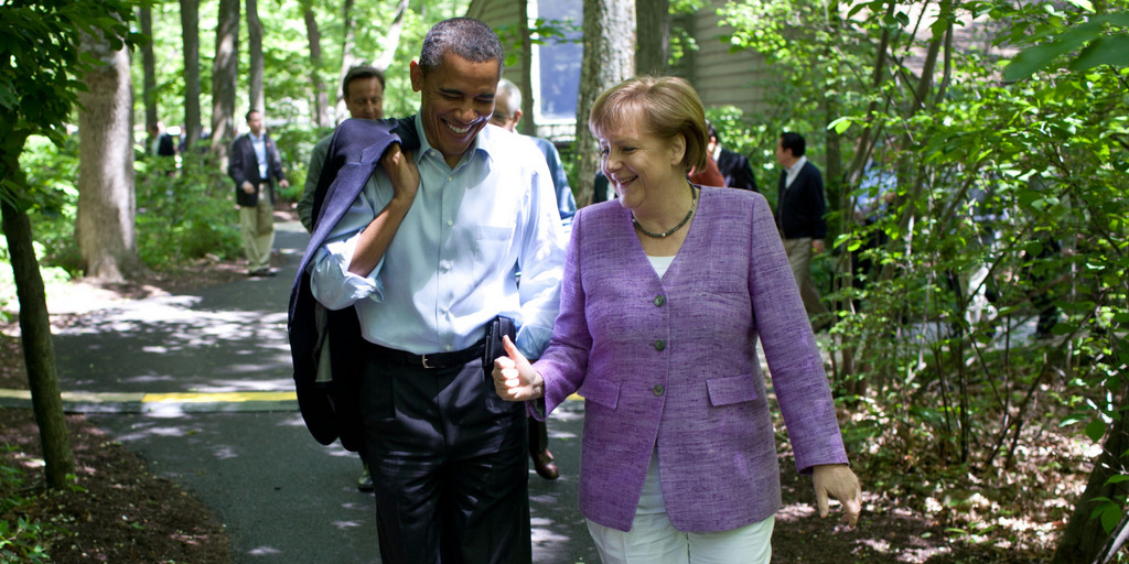 US President Barack Obama and German Chancellor Angela Merkel take a walk on the compound of Camp David, the President's country retreat. Obama and Merkel are engaged in a conversation and smile.