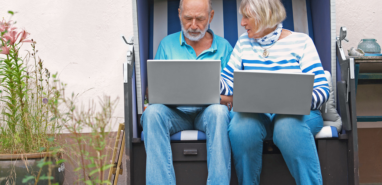 (© Arne Weychardt) Seniorenpaar sitzt in Strandkorb und schaut auf Laptops
