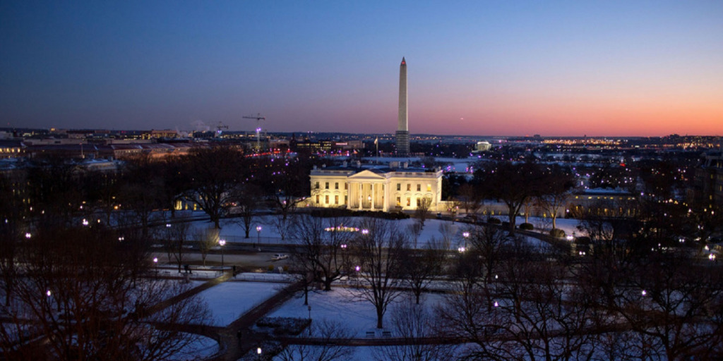 The illuminated White House in Washington, DC in dusk on a snowy winter evening. In the background one can see the obelisk of the Washington Monument.