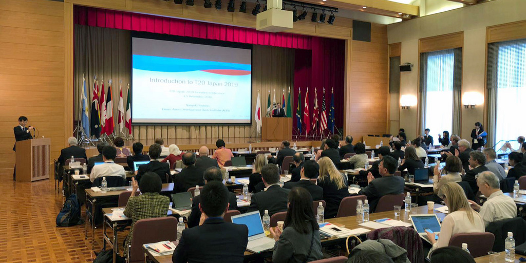 T20 Konferenz in Tokio, viele Leute in einem großen Raum, die auf eine Leinwand starren, auf der eine Präsentation läuft.