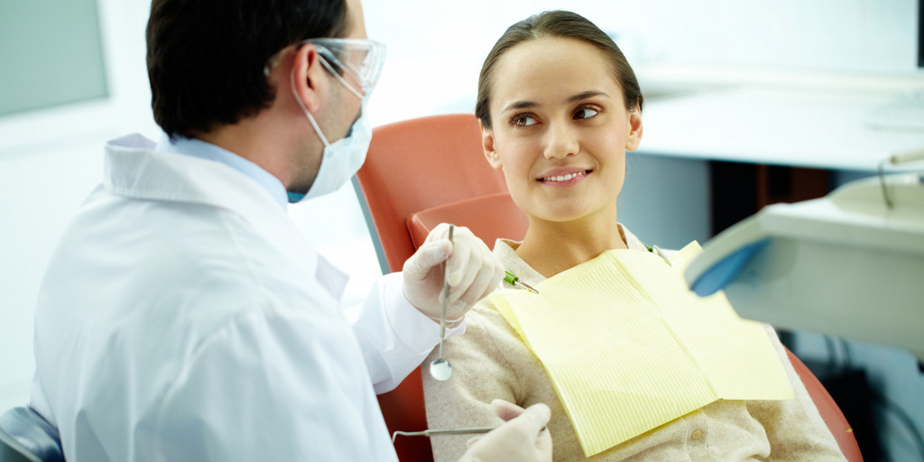 Eine Frau sitzt beim Zahnarzt und lächelt ihren Arzt an 