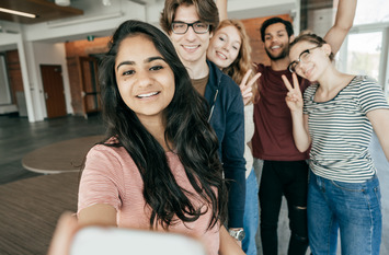 Mehrere junge Menschen nehmen mit einem Handy ein gemeinsames Selfie auf und lächeln in die Kamera.