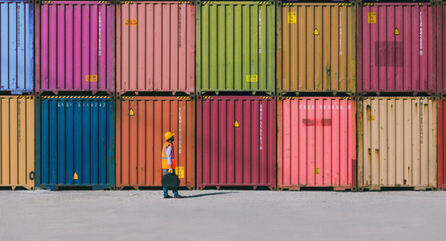 Engineer man with yellow crash helmet and worker west checking cargo freights in front of colorful cargo container stacks in shipping port