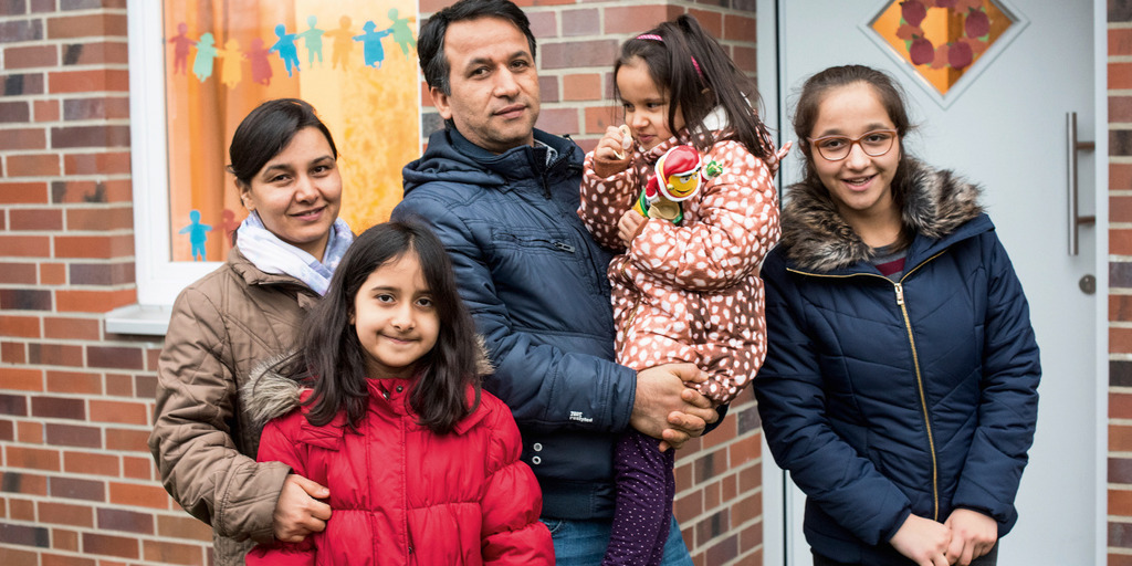 [Translate to English:] Eine fünfköpfige Familie - Eltern und drei Töchter - steht vor ihrem Wohnhaus.