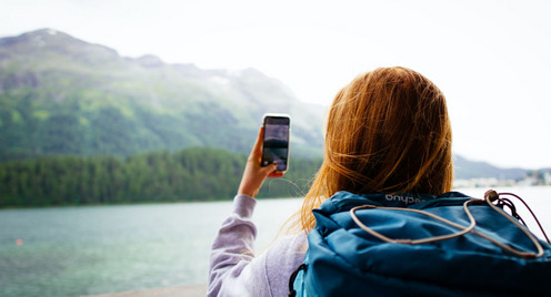 Junge Frau fotografiert einen Berg, im Vordergrund ist ein See zu sehen.