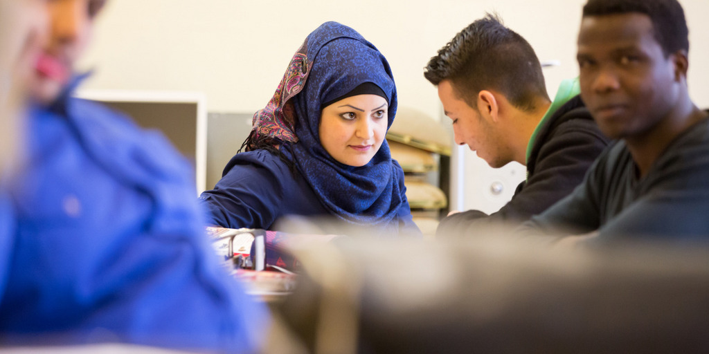 Mehrere Flüchtlinge sitzen in Raum einer berufsbildenden Schule in Lüchow. Zwei unterhalten sich, einer blickt direkt in die Kamera.