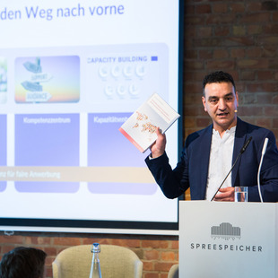 Najim Azahaf von der Bertelsmann Stiftung präsentiert dem Publikum die Abschlusspublikation „Fachkräftemigration fair gestalten durch transnationale Skills Partnerships