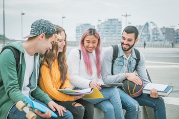 Vier junge Menschen sitzen und schauen sich gemeinsam und fröhlich Studienunterlagen an.