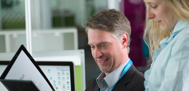 Ein Mann und eine Frau stehen in einem Büroraum und blicken in auf ein Schriftstück in einer Arbeitsmappe.A man and a woman a standing in a bureau looking on a script in a map.